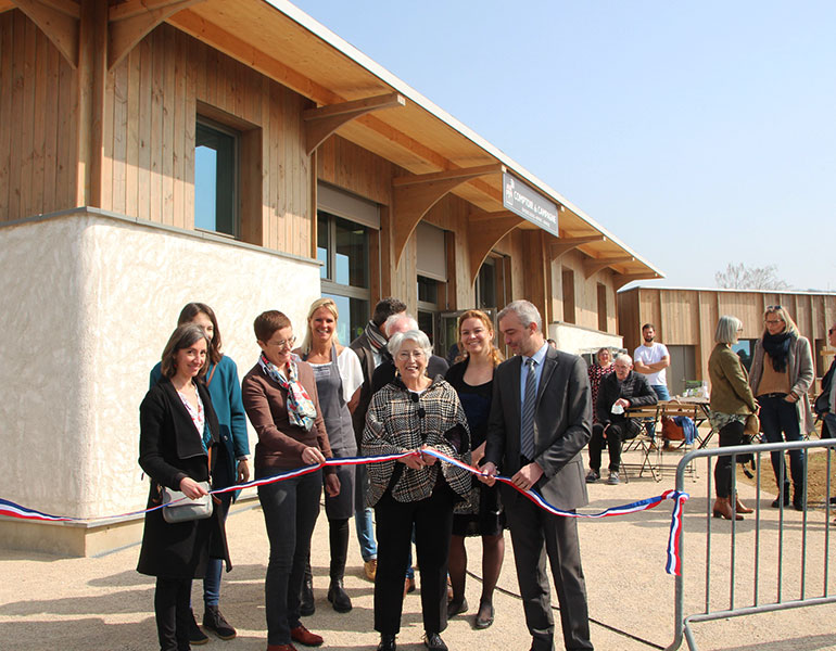Un groupe de personnes sourient et tiennent un ruban et une personne au centre de l'image coupe le ruban 